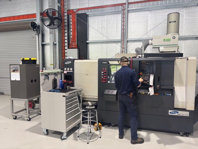 Technician operating CNC machining center in a modern industrial workshop with tools and equipment